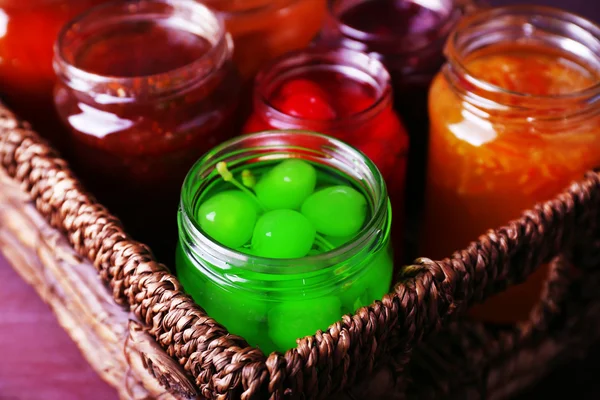 Zelfgemaakte potten van vruchten jam in rieten mand en kleur houten achtergrond — Stockfoto