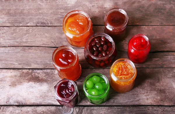 Homemade jars of fruits jam on rustic wooden background — Stock Photo, Image