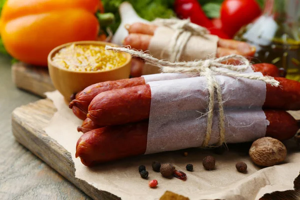 Assortiment de saucisses fines, moutarde dans un bol et épices sur planche à découper, sur fond bois — Photo