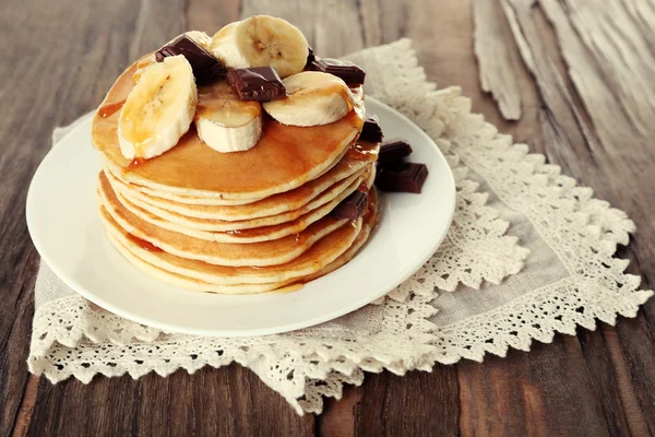 Stapel van heerlijke pannenkoeken met chocolade, honing en segmenten van banaan op plaat en servet op houten tafel achtergrond — Stockfoto