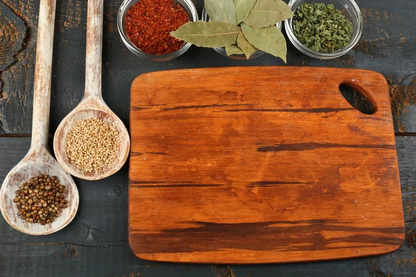 Différentes épices et herbes avec planche à découper sur fond de table en bois couleur — Photo