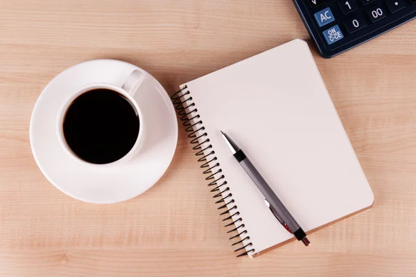 Taza de café en platillo con cuaderno, calculadora y pluma sobre fondo de mesa de madera —  Fotos de Stock