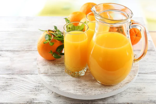 Glass of orange juice and oranges on color wooden table background — Stock Photo, Image