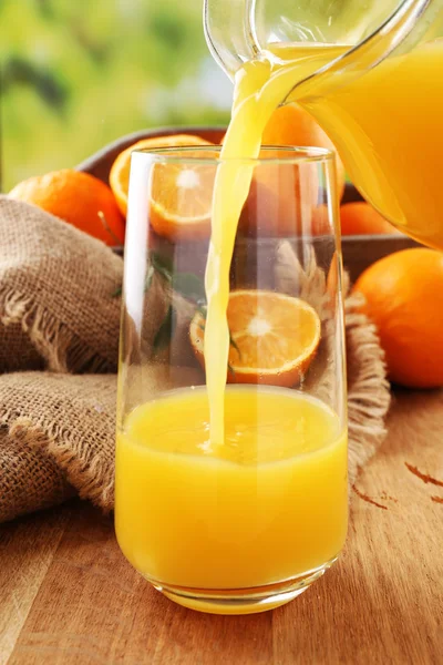 Pouring orange juice from glass carafe, on wooden table and bright background — Stock Photo, Image