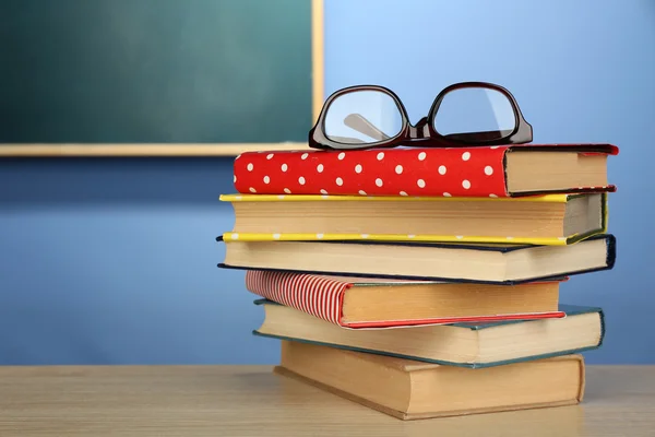 Pila di libri con vetri su scrivania in legno, su parete colorata e sfondo lavagna — Foto Stock