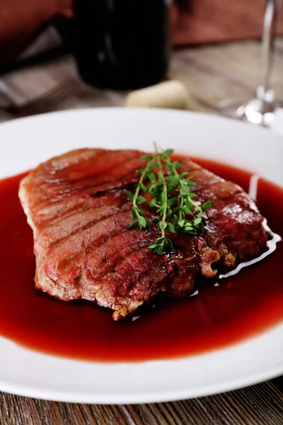 Gegrilde steak in wijnsaus met fles wijn op houten achtergrond — Stockfoto