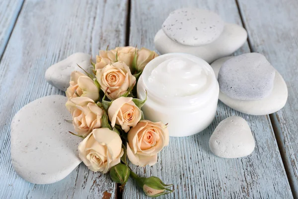 Crema cosmética con flores y piedras de spa sobre fondo de madera — Foto de Stock