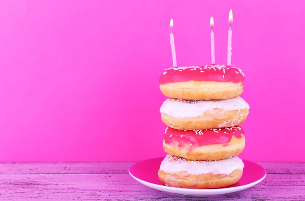 Délicieux beignets avec glaçage et bougies d'anniversaire sur la table sur fond lumineux — Photo