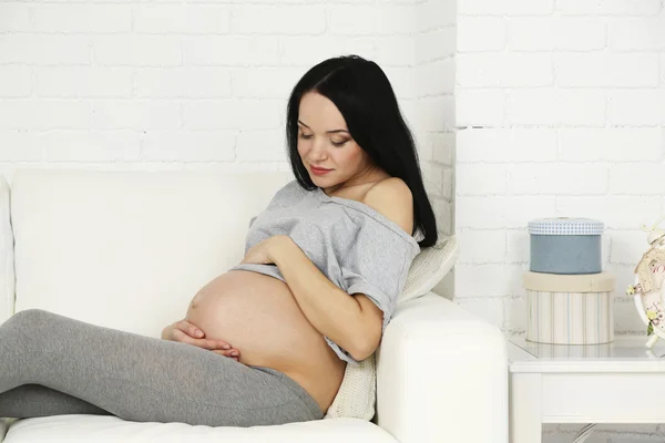 Wanita hamil muda santai di sofa dengan latar belakang interior rumah — Stok Foto