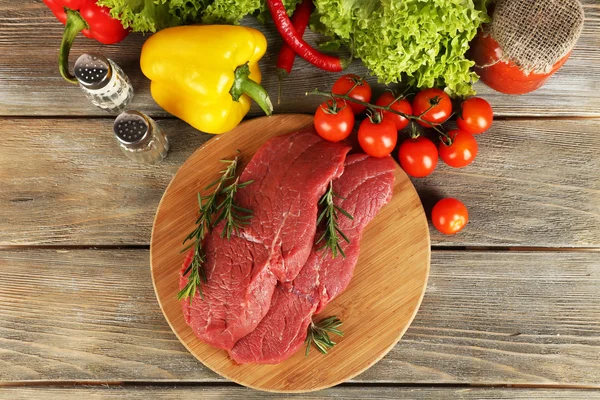 Rauwe biefstuk op snijplank met groenten en specerijen op houten achtergrond — Stockfoto