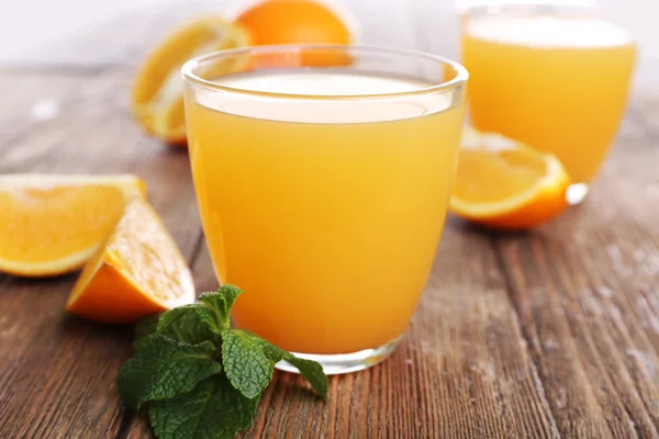 Ποτήρια χυμό πορτοκαλιού με τα πορτοκάλια σε ξύλινα πίνακα από κοντά — Φωτογραφία Αρχείου