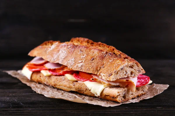 Свежий и вкусный сэндвич с ветчиной и сыром на бумаге на деревянном фоне — стоковое фото