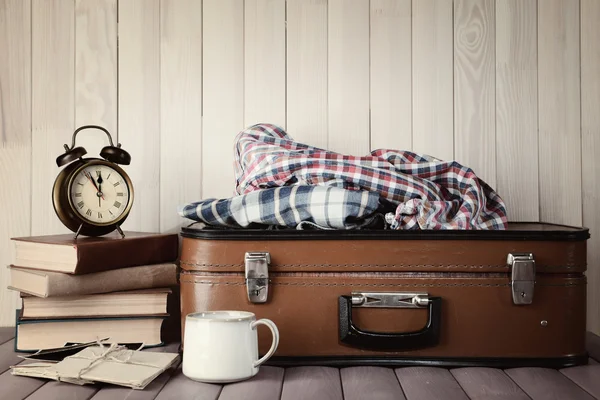 Maleta vintage con ropa y libros sobre fondo de madera — Foto de Stock