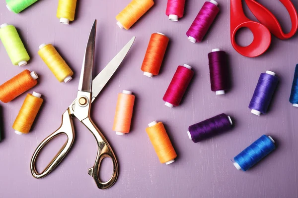 Multicolor sewing threads with scissors on wooden background — Stock Photo, Image