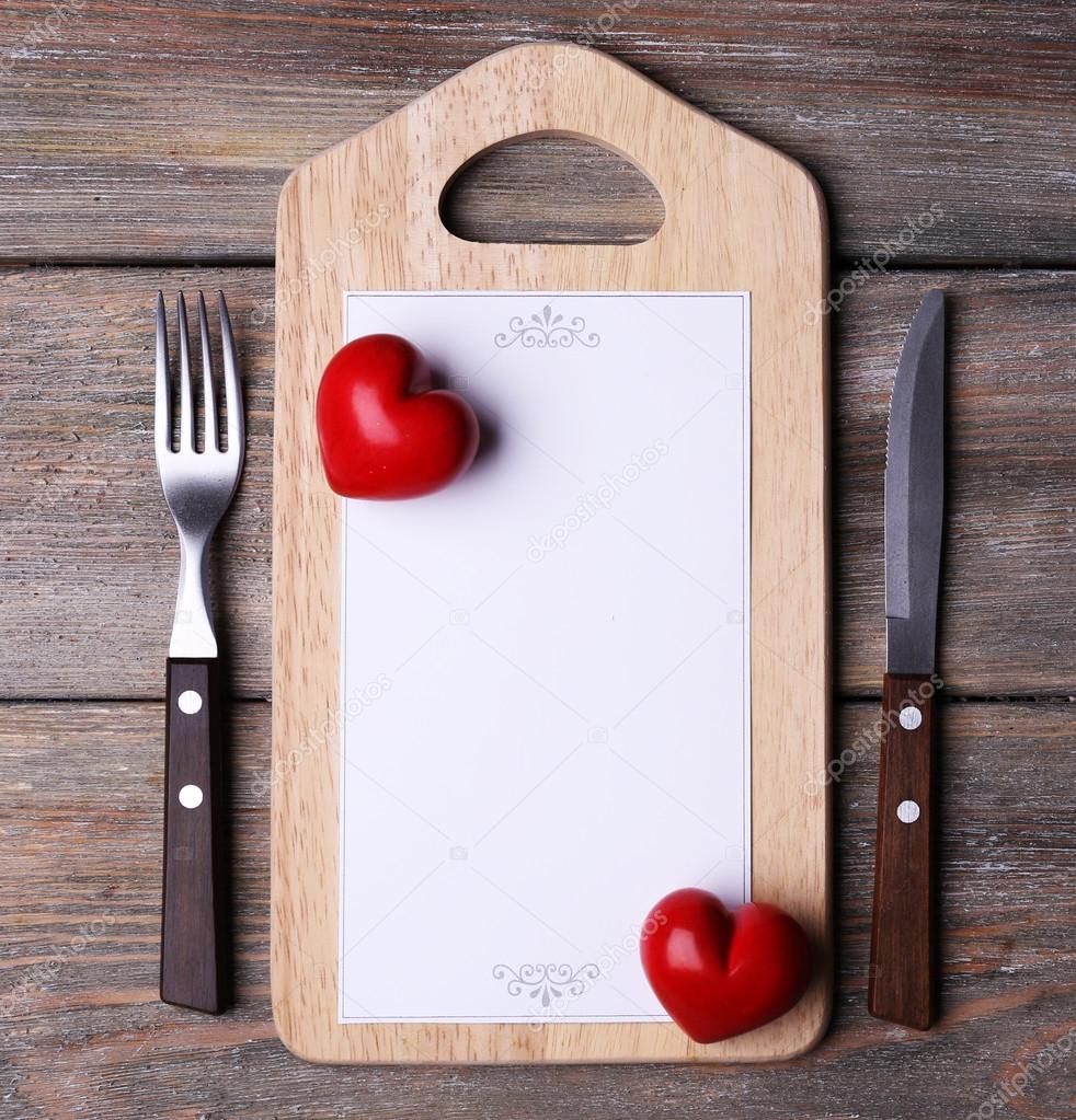 Cutting board with menu sheet of paper and hearts on rustic wooden planks background