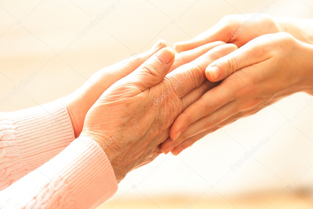 Old and young holding hands on light background, closeup