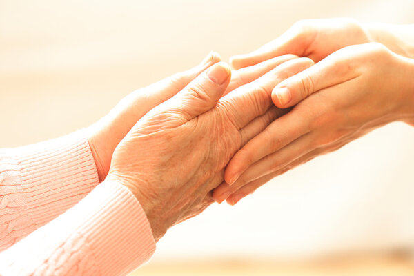 Old and young holding hands on light background, closeup