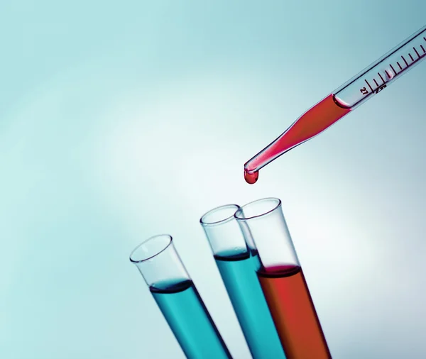 Pipette adding fluid to the one of test-tubes on light background — Stock Photo, Image