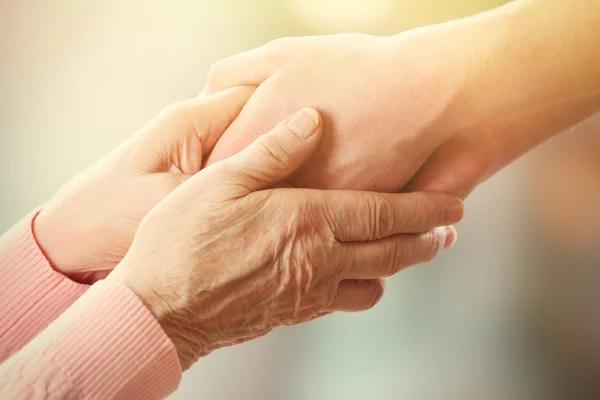 Old and young holding hands on light background, closeup — Stock Photo, Image