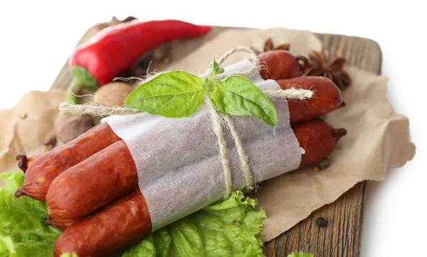 Salsichas finas defumadas com folhas de salada de alface e especiarias em tábua de corte de madeira, isoladas em branco — Fotografia de Stock