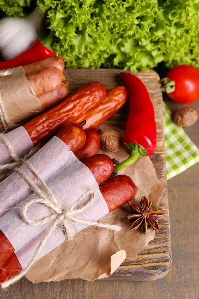Ассортимент тонких колбас, горчицы в миске и специй на разделочной доске, на деревянном фоне — стоковое фото