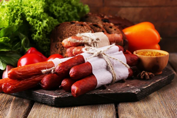 Assortimento di salsicce sottili, pane, senape in ciotola e spezie su tagliere, su fondo di legno — Foto Stock