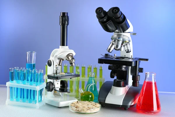 Microscopen en reageerbuizen op tafel, op kleur achtergrond — Stockfoto