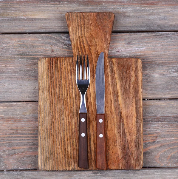 Tabla de cortar con tenedor y cuchillo sobre fondo rústico de tablones de madera —  Fotos de Stock