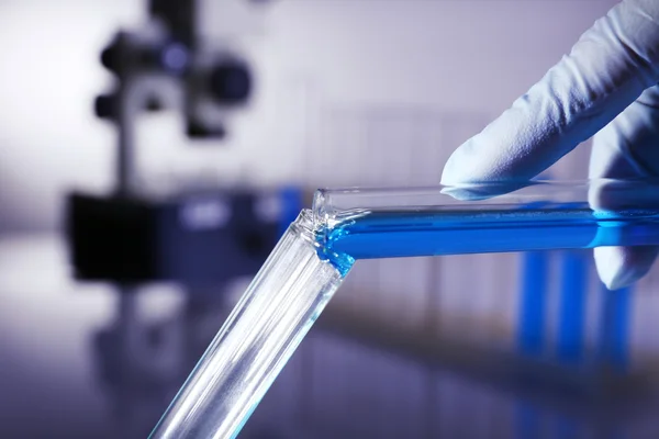 Лабораторное стекло с голубой жидкостью в руке ученого на сером фоне — стоковое фото