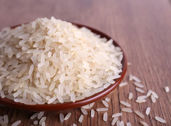 Grain of rice on plate on wooden background — Stock Photo, Image