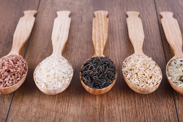 Diferentes tipos de arroz em colheres no fundo de madeira — Fotografia de Stock