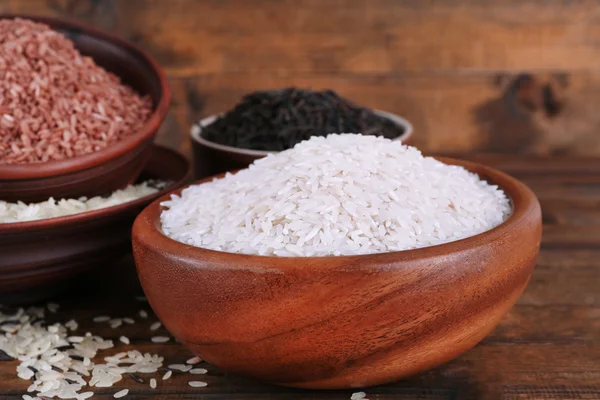 Diferentes tipos de arroz em tigelas em fundo de madeira — Fotografia de Stock