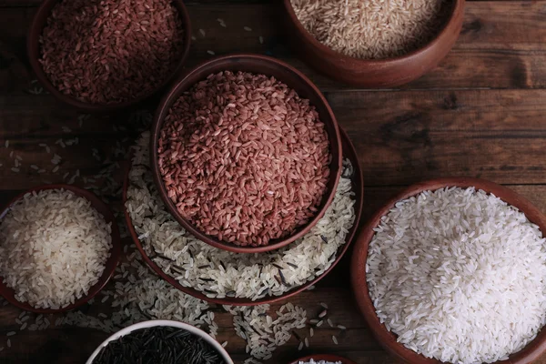 Ahşap arka plan üzerinde kase pirinç çeşitleri — Stok fotoğraf