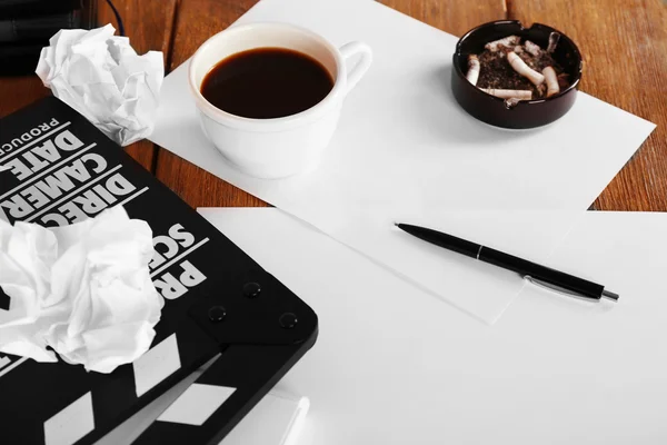 Moving clapper with sheets of paper, ashtray, cup of coffee and pen on wooden planks background — Stock Photo, Image