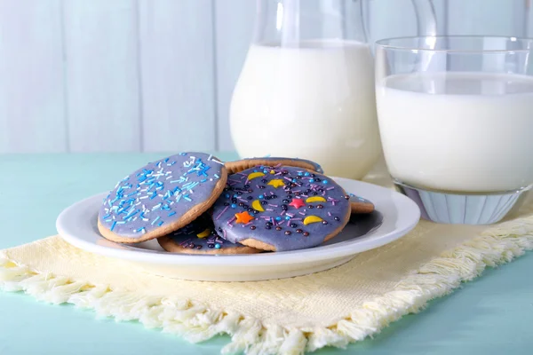 Biscotti glassati con vetro e brocca di latte su sfondo di legno a colori — Foto Stock