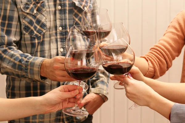 Clinking glasses of red wine in hands on color wooden planks background — Stock Photo, Image