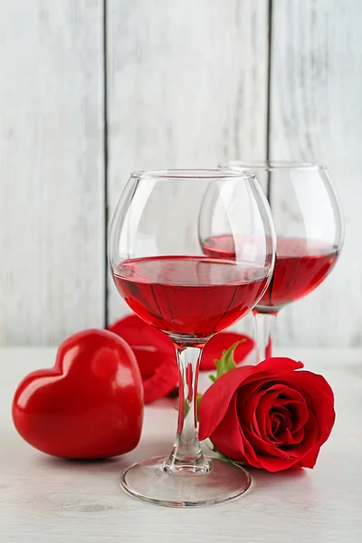 Composition avec vin rouge en verre, roses rouges et coeur décoratif sur fond de bois de couleur — Photo