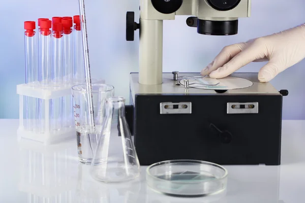 Hand of assistant in gloves working with microscope near test tubes on blurred background — Stock Photo, Image