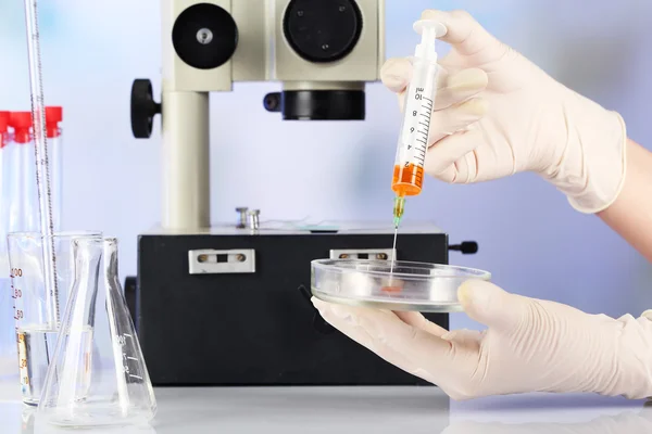 Assistant hands in gloves making analysis in laboratory with microscope and blurred background — Stock Photo, Image