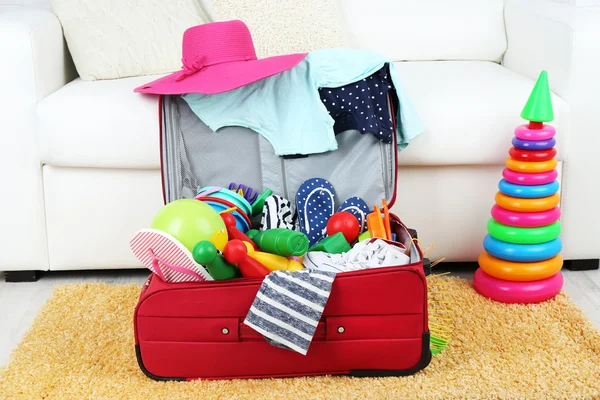 Suitcase packed with clothes and child toys on fur rug and white sofa background — Stock Photo, Image