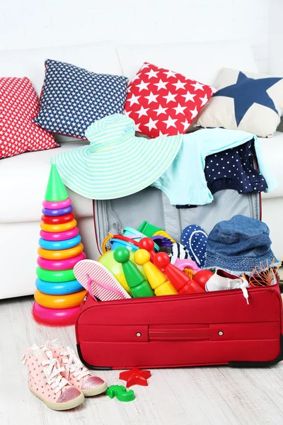 Koffer voller Kleidung und Kinderspielzeug auf Holzboden und weißem Sofa-Hintergrund — Stockfoto