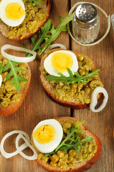 Smörgåsar med gröna ärtor pasta och kokt ägg med lökringar och citron på träplankor bakgrund — Stockfoto