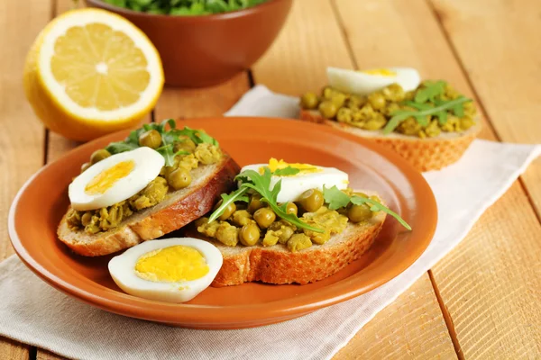 Sandwiches with green peas paste and boiled egg on plate with napkin on wooden planks background — Stock Photo, Image