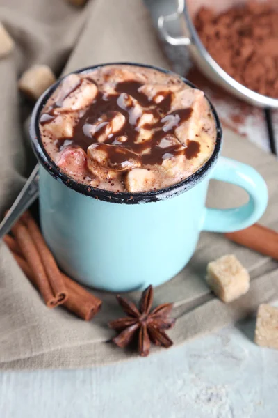 Taza de café caliente con malvavisco en tela con azúcar en bulto, canela, anís estrellado y tinte de cacao sobre fondo de tablones de madera de color — Foto de Stock