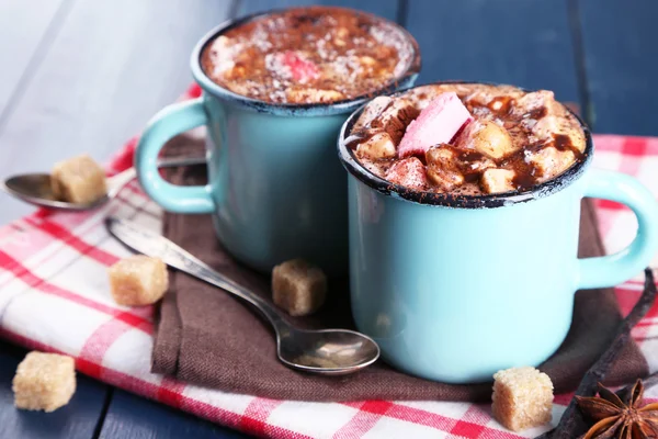 Tazas de café caliente con malvavisco en la servilleta con azúcar en bulto, anís estrellado y palos de vainilla en el fondo de mesa de madera de color — Foto de Stock