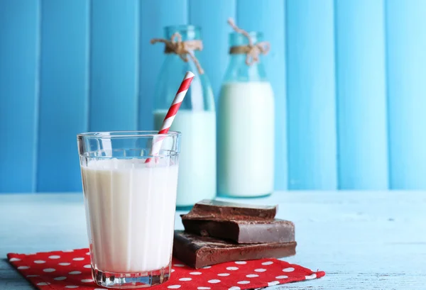 Vaso y botellas de leche con trozos de chocolate en la servilleta de puntos y fondo de tablones de madera de color — Foto de Stock