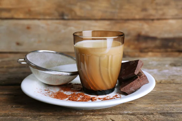 Bicchiere di latte con pezzi di cioccolato e cacao su sfondo rustico di tavole di legno — Foto Stock