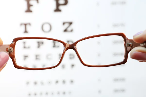 Gafas para ojos en manos femeninas en el fondo de la tabla de pruebas de la vista — Foto de Stock