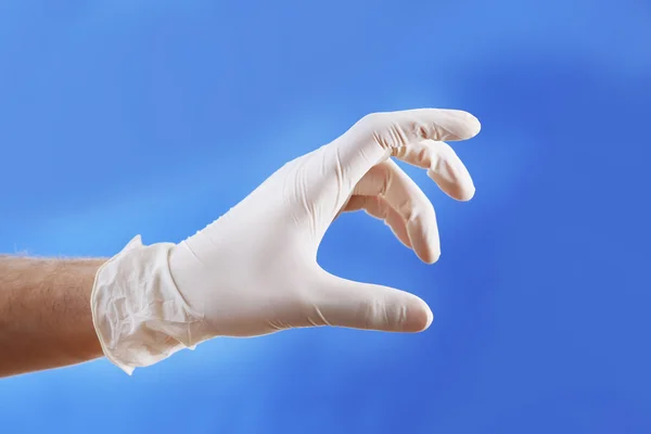 Main de médecin en gants stériles sur fond bleu — Photo