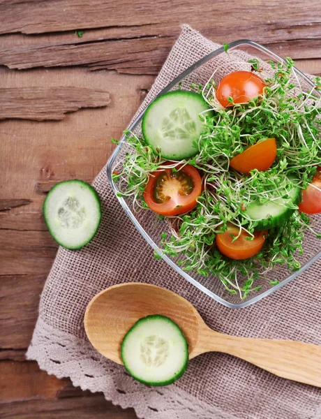 Salada de agrião com pepino fatiado e tomate cereja em tigela de vidro no fundo da mesa de madeira rústica — Fotografia de Stock